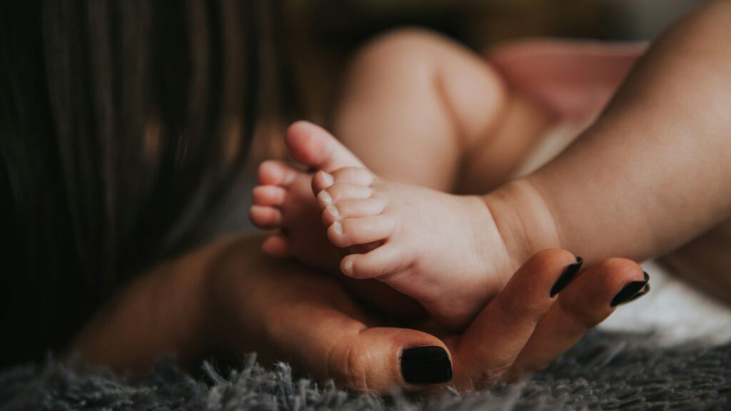 A close-up of an adult hand gently cradling the tiny feet of a baby, capturing a tender and intimate moment of care and connection.